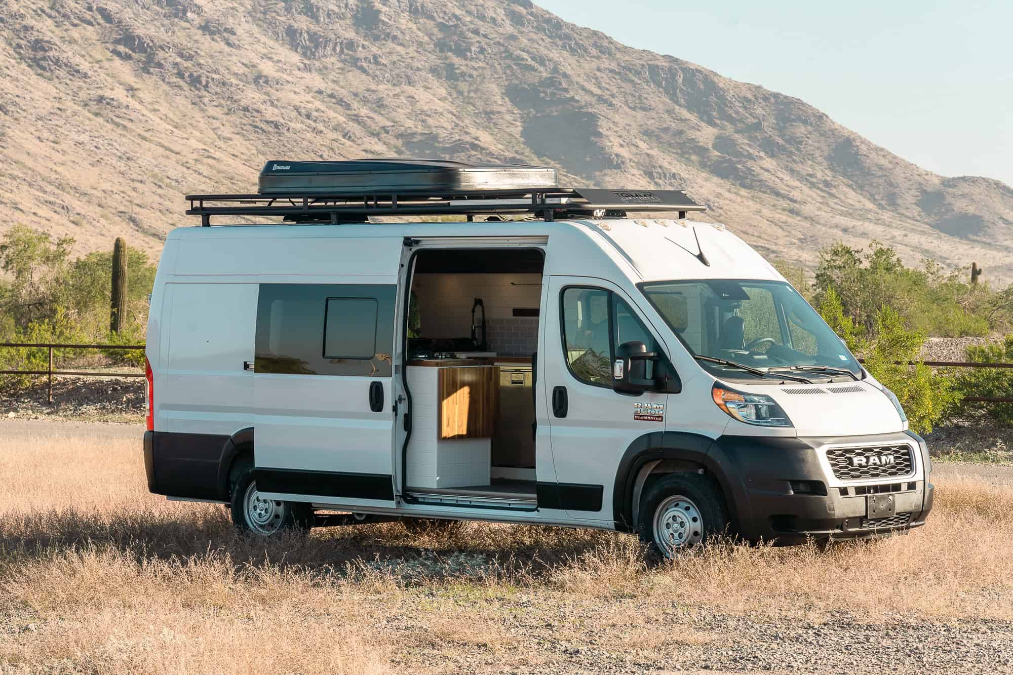 Three-quarter front view of the Tommy Camper Vans ProMaster showing the hard-shell rooftop tent and roof rack