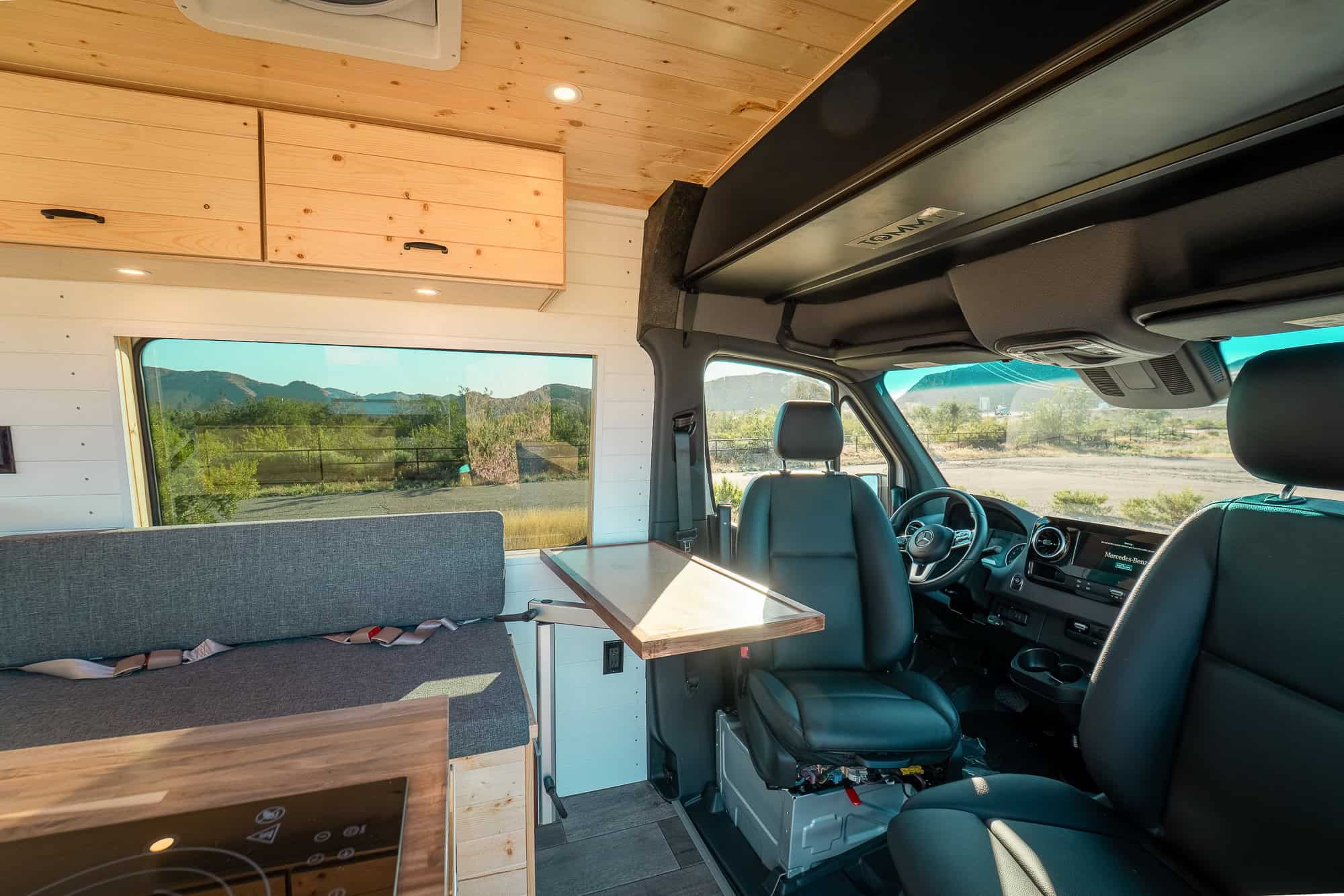 Grey upholstered belted bench and fold-out table facing the swiveled cab seats in the Sprinter
