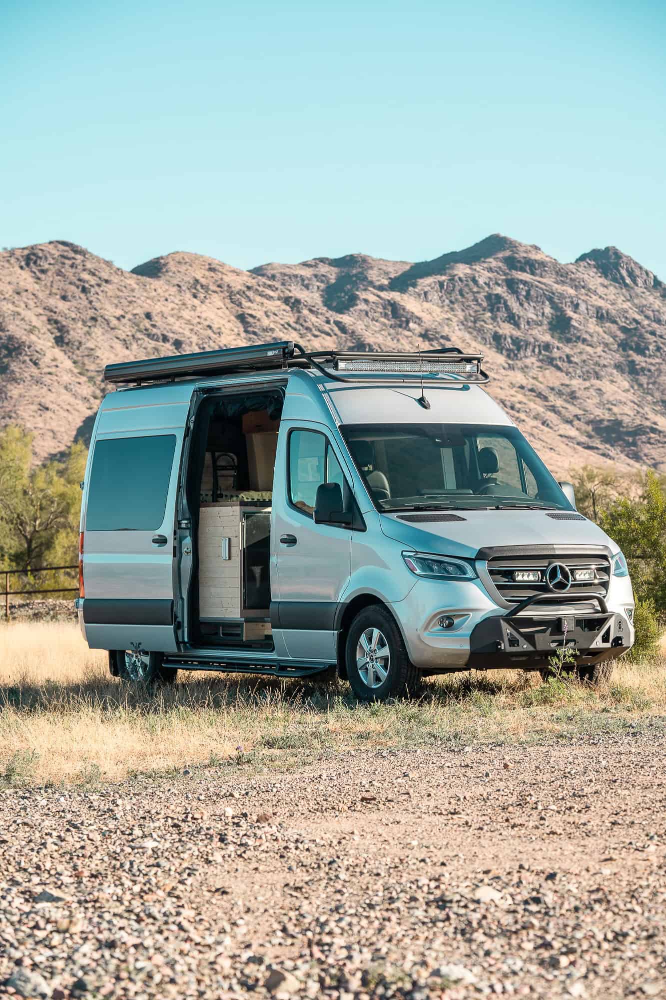 Silver 2024 Mercedes Sprinter camper van by Tommy Camper Vans with sliding door open in the Arizona desert
