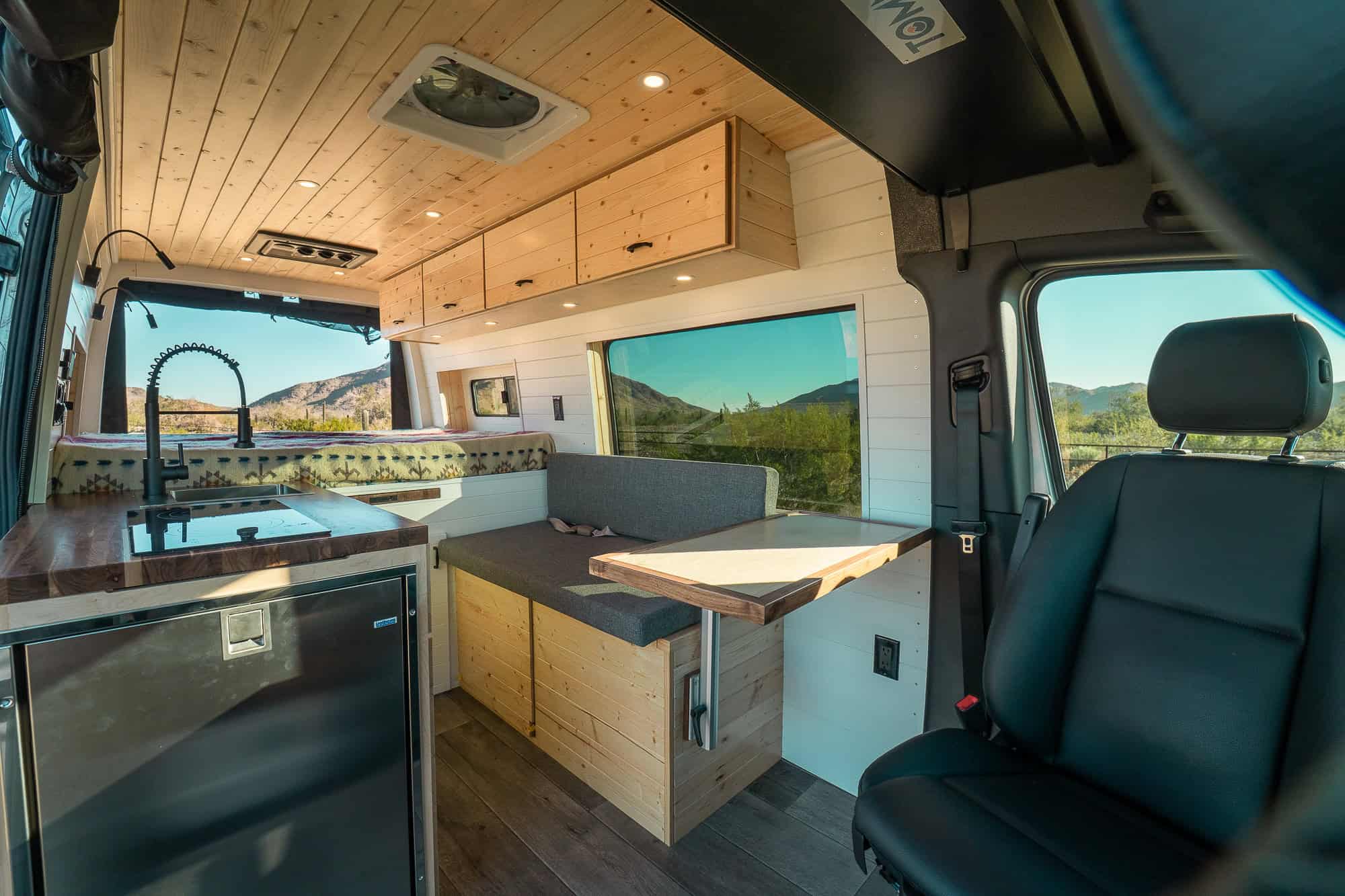 Interior of the Bennett layout Sprinter looking rearward past the induction cooktop and dinette toward the fixed bed