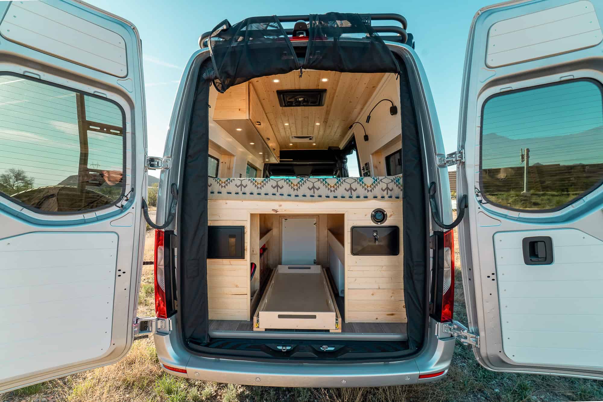 Rear doors open showing the garage beneath the bed with a slide-out cargo tray and exterior shower port