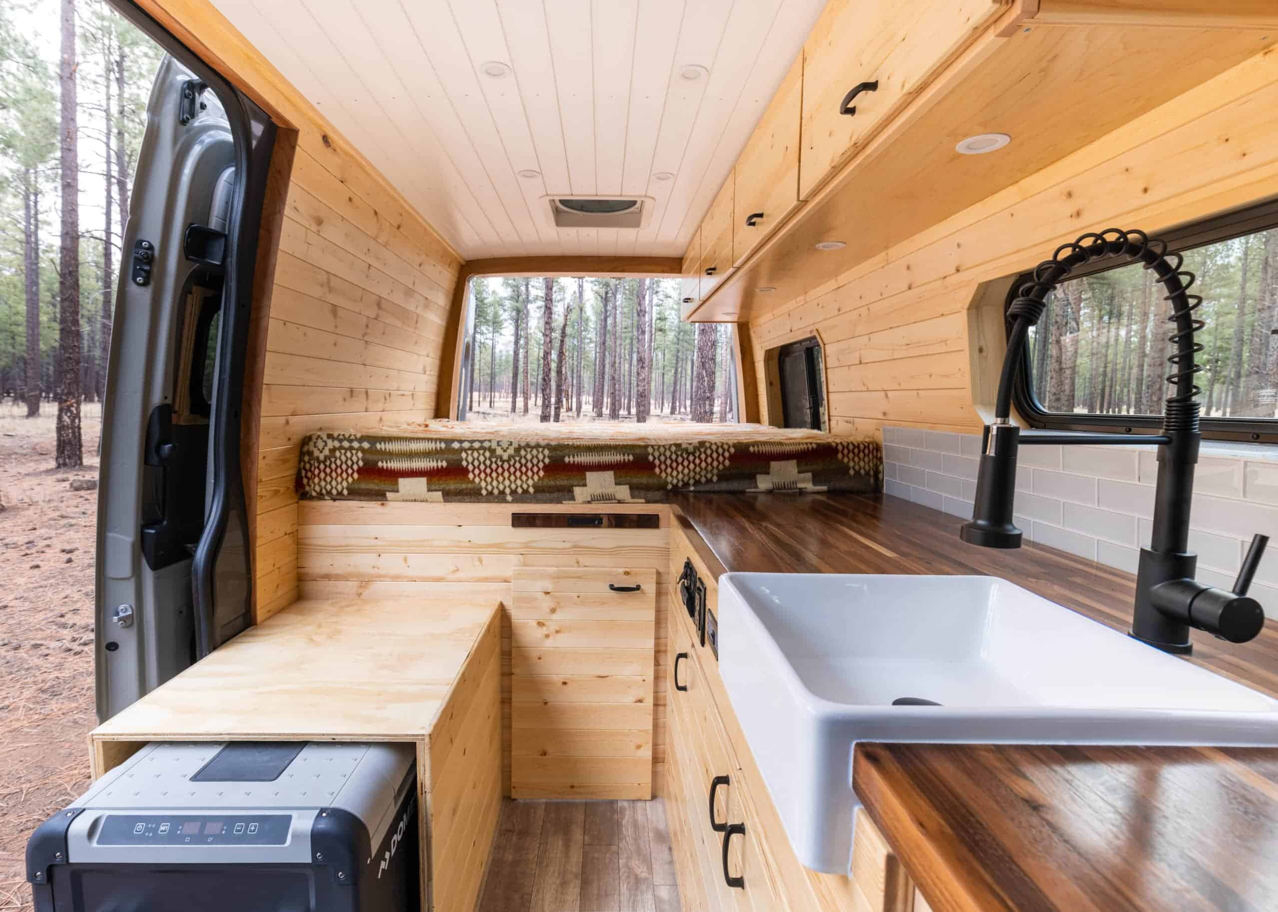 Knotty pine Bennett layout interior with rear bed, walnut counter, farmhouse sink and a Dometic cooler in the bench