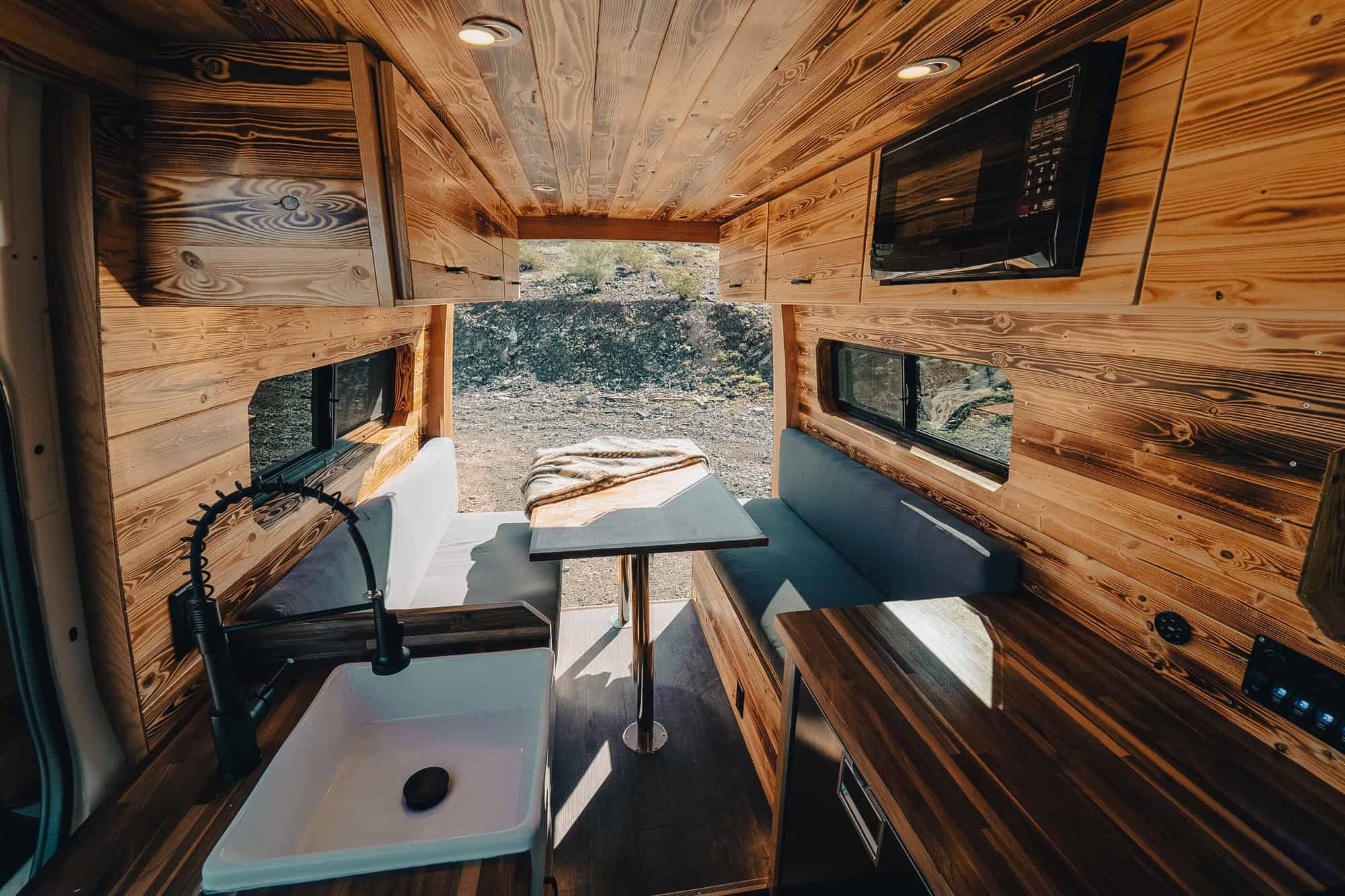 Burnt wood Convertible Dinette interior with two facing bench sofas, a pedestal dining table and a microwave