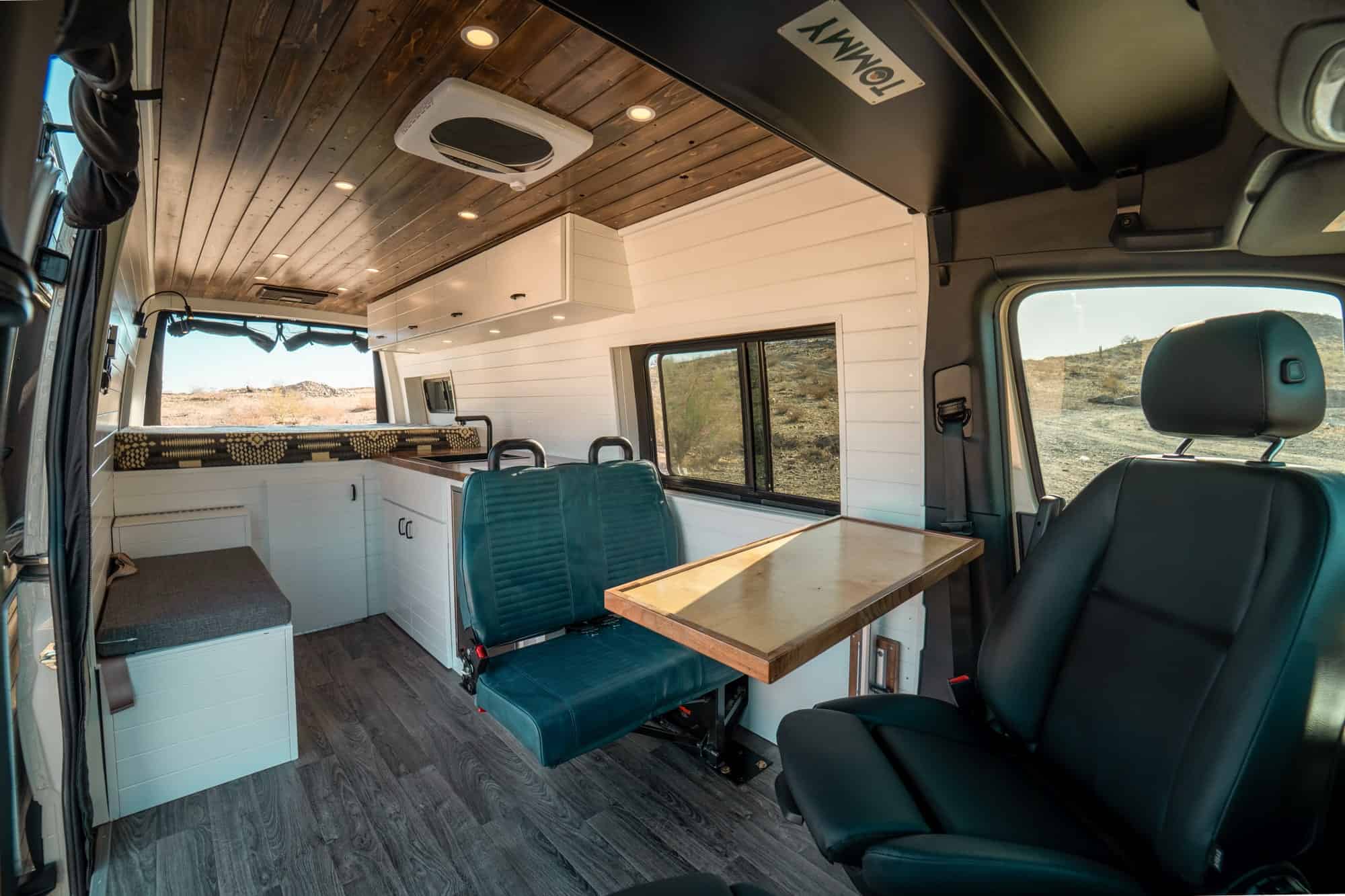 White Jump Seat layout interior with a teal belted bench, wood table and rear fixed bed