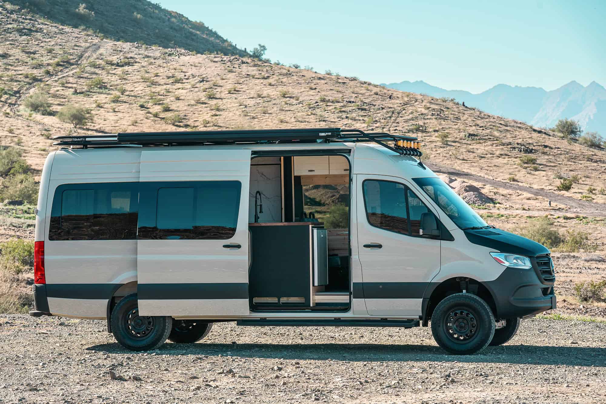 Exterior side view of a Tommy Camper Vans MAV on a 170-inch Sprinter with roof rack, awning and all-terrain tires