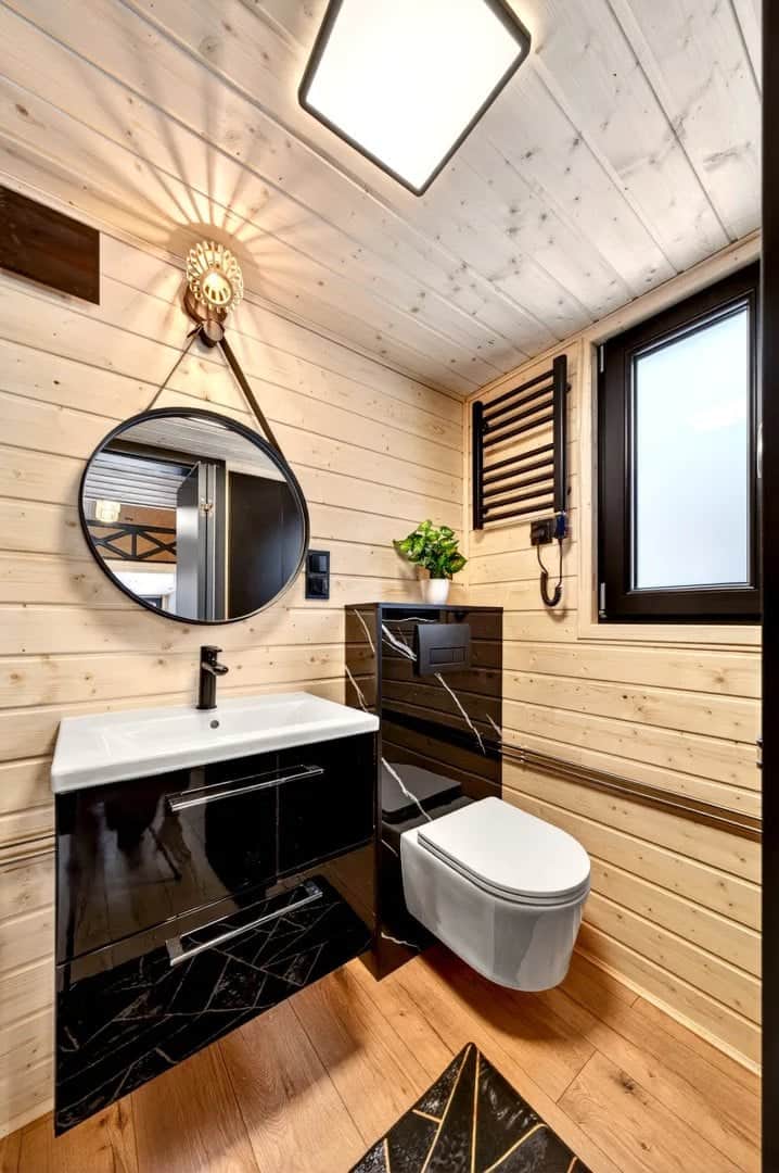 Tommy tiny house bathroom with spruce walls, a round mirror, a black vanity, and a towel radiator