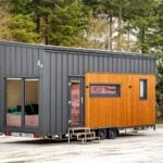 The Tommy tiny house by Craft House with dark standing-seam metal and thermo-pine wood siding parked in a snowy forest