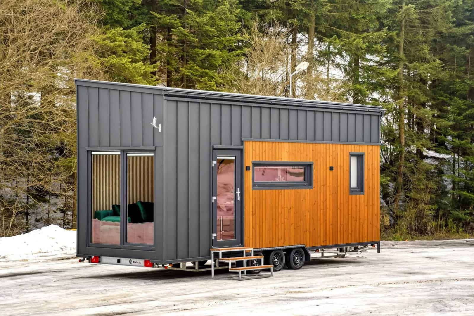 The Tommy tiny house by Craft House with dark standing-seam metal and thermo-pine wood siding parked in a snowy forest