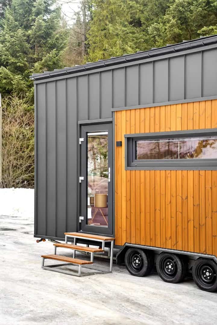 Entry door and steps of the Tommy tiny house beside its dark standing-seam metal facade