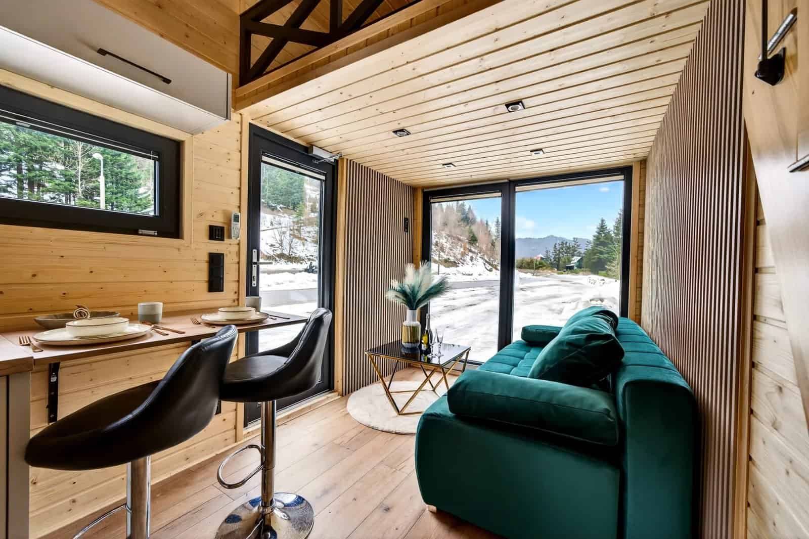 Living room of the Tommy tiny house with a green velvet sofa, dining bar, and glass doors to a mountain view
