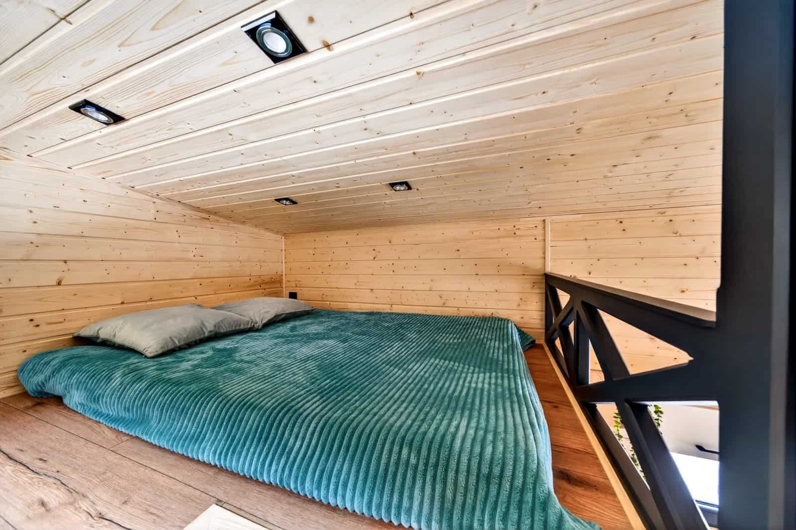 Mezzanine bedroom in the Tommy tiny house with a double bed under a spruce ceiling