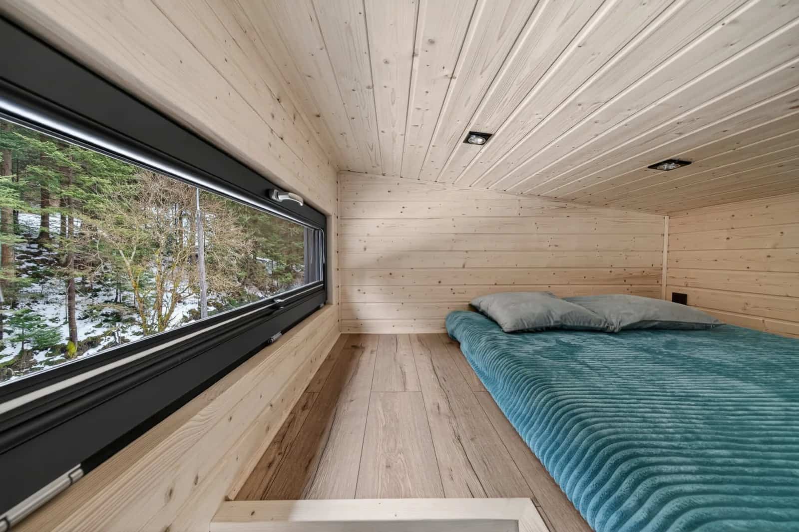 Mezzanine sleeping loft in the Tommy tiny house with a long window overlooking the forest