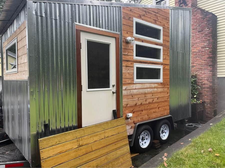 Tiny house on wheels with metal siding and wooden accents, designed for affordable living and mobili.