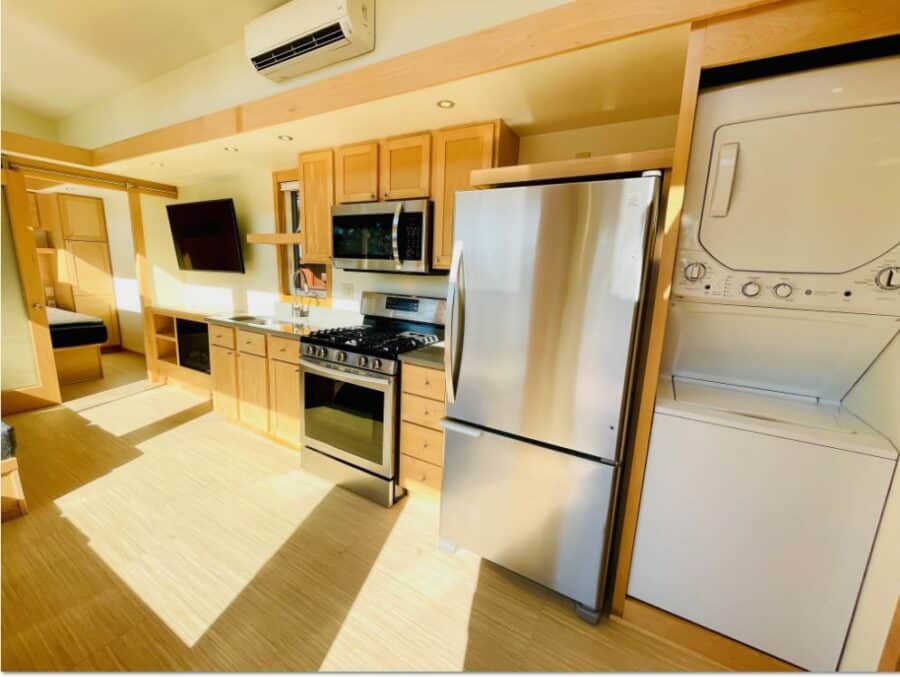 Modern tiny house kitchen with stainless steel appliances and wooden cabinets.