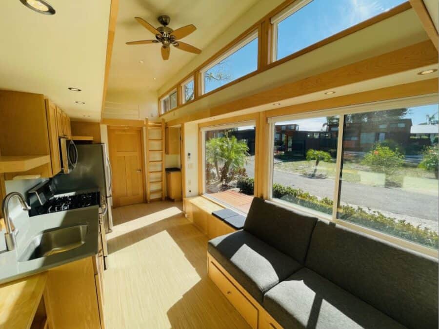 Bright, open-plan tiny house with large windows and modern kitchen design.