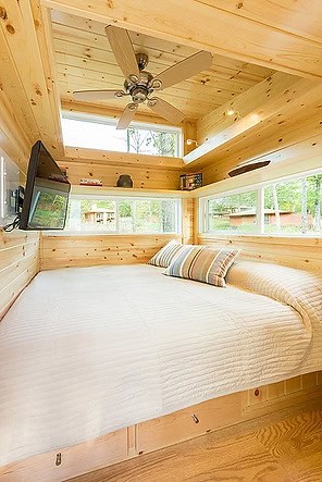 Small wooden tiny house bedroom with large windows and lake view.