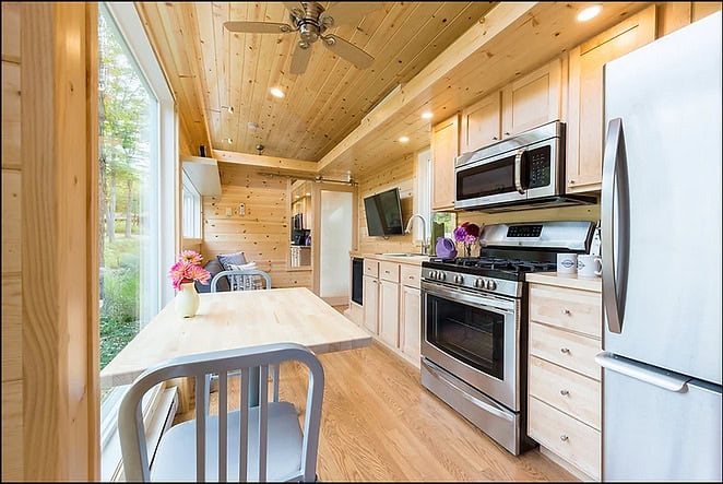 Bright tiny house kitchen with lake view and natural wood interior.