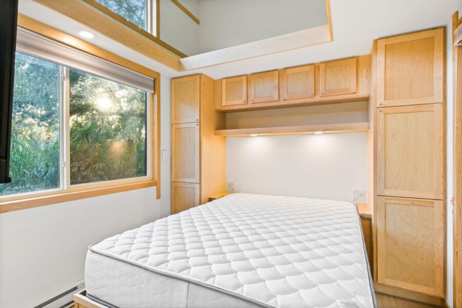 Cozy tiny house bedroom featuring built-in wooden cabinets and a large window with natural light.