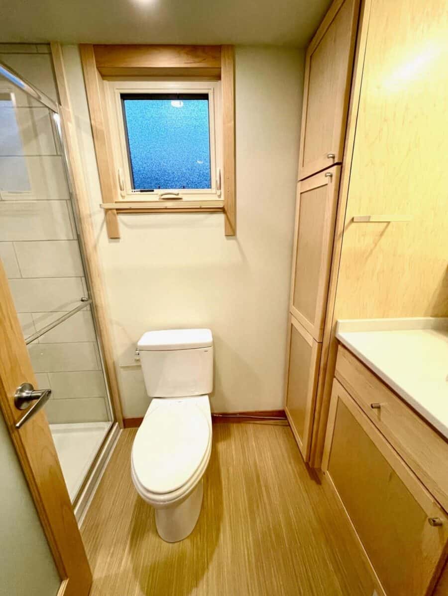 Bathroom in tiny house with wooden cabinetry and a small window for natural light.