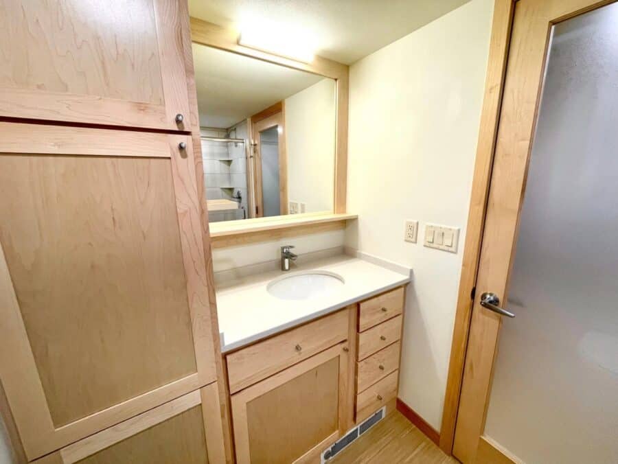 Compact bathroom in a tiny house featuring wooden cabinetry and a large mirror.