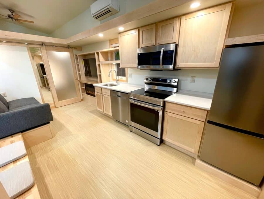 Tiny house kitchen with modern appliances and light wood cabinets.