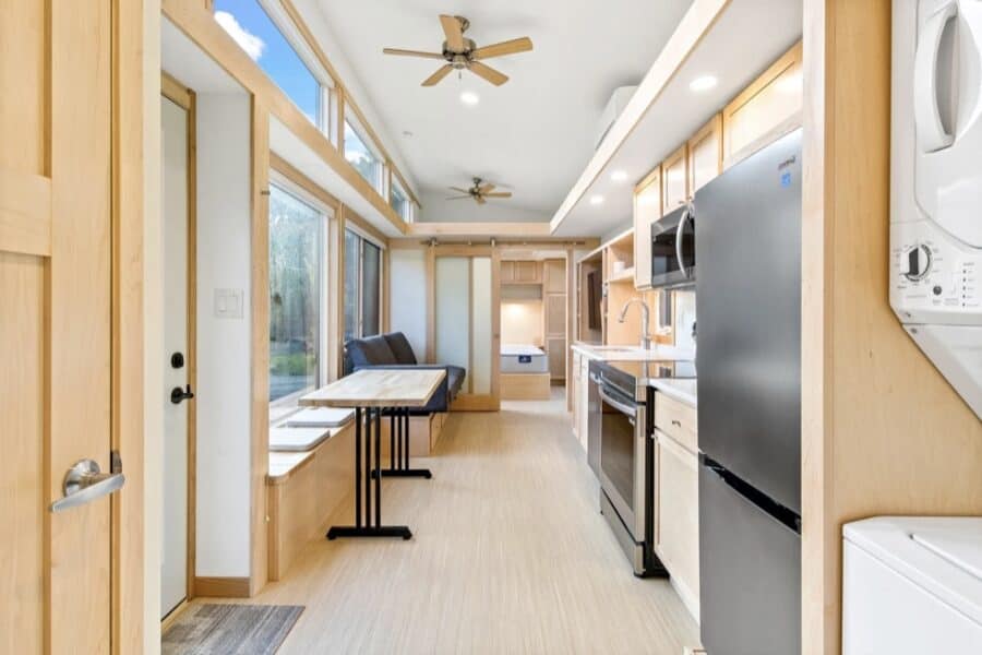 Interior view of a tiny house with a modern kitchen, large windows, and natural light.