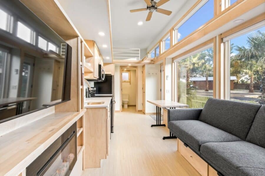 Modern tiny house interior with wide windows, cozy sofa, and compact kitchen for comfortable living.