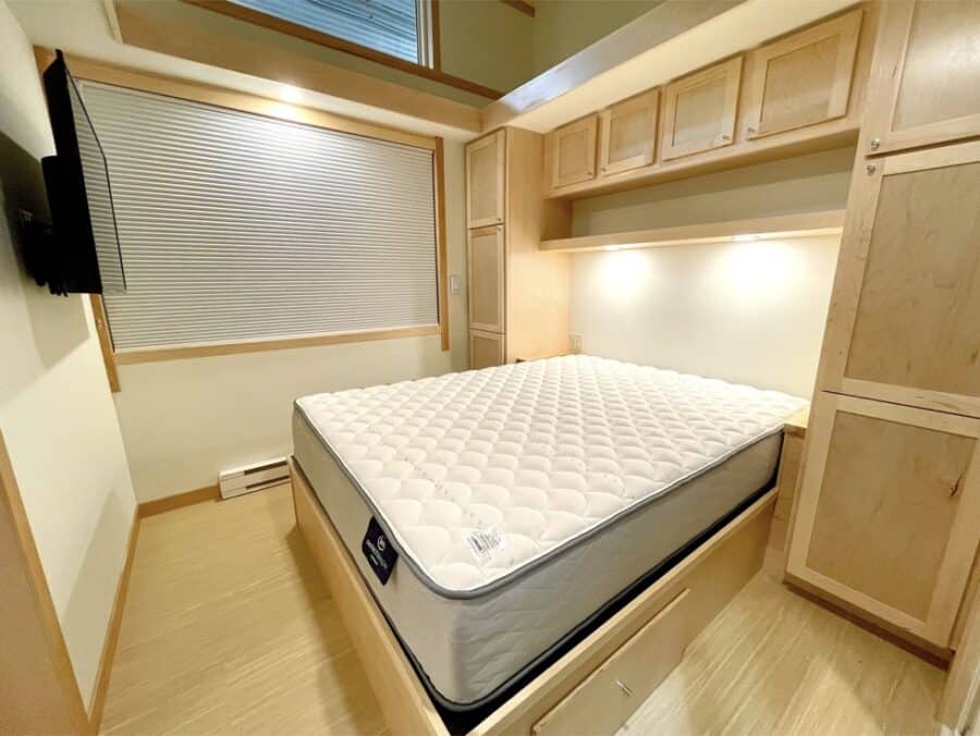 Compact tiny house bedroom with a comfortable mattress and custom storage cabinets.