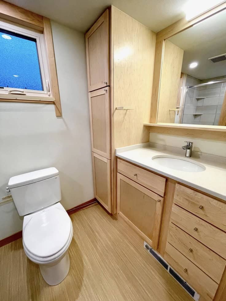 Bathroom in tiny house with wooden cabinetry, compact sink, and small window for natural light.