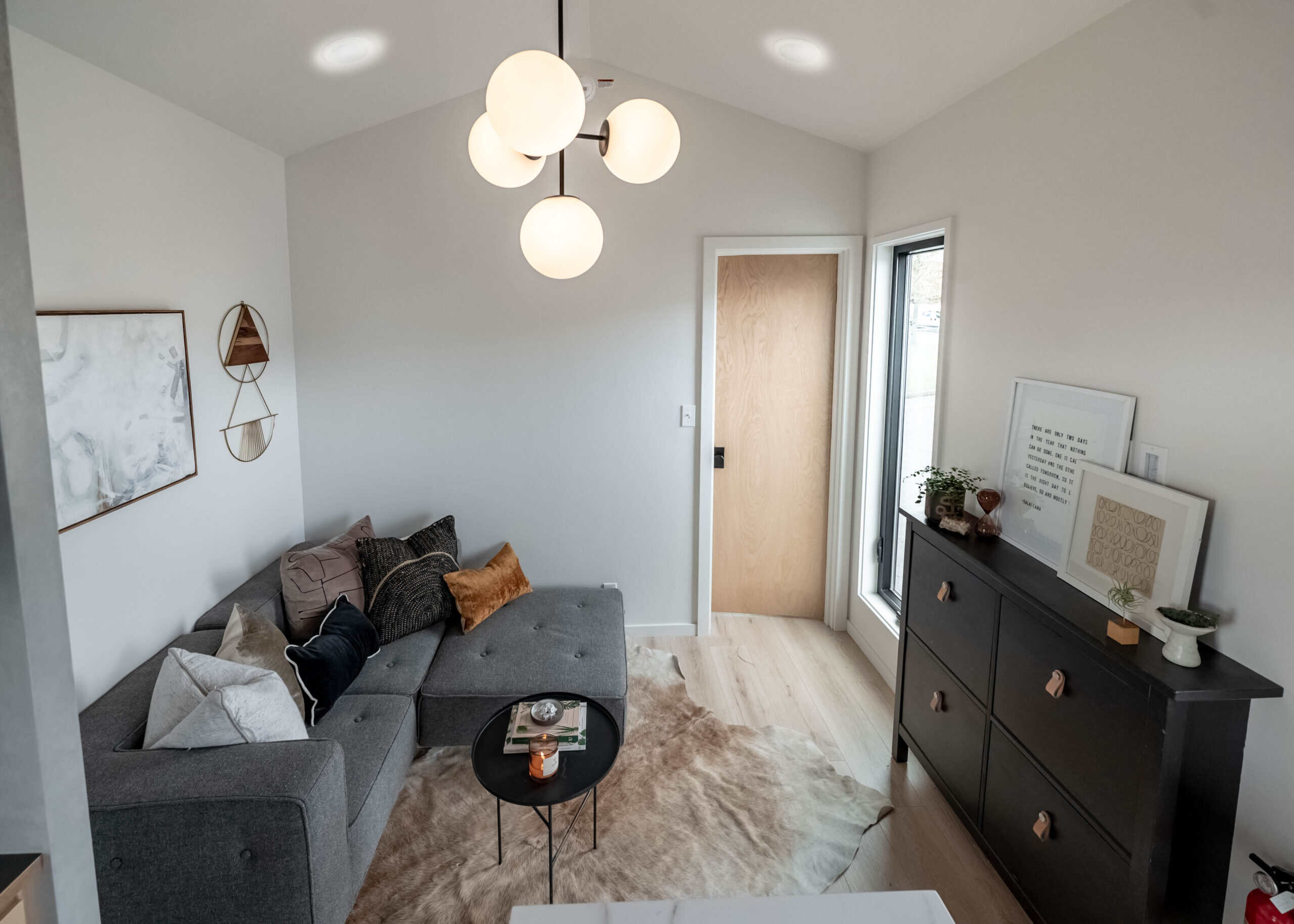 Living area from another angle showing drywall walls, art, dresser, and hallway to bedroom