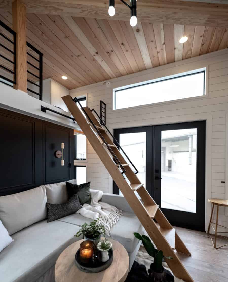 Interior view of a modern tiny house with a loft and large windows.