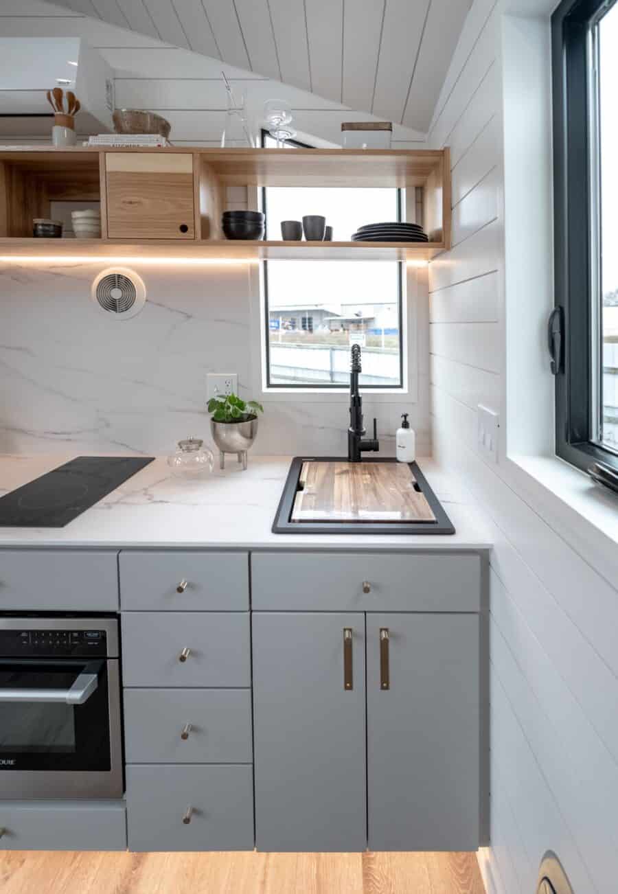 Modern tiny house kitchen with sleek white cabinets, wooden accents, and a large window for natural.