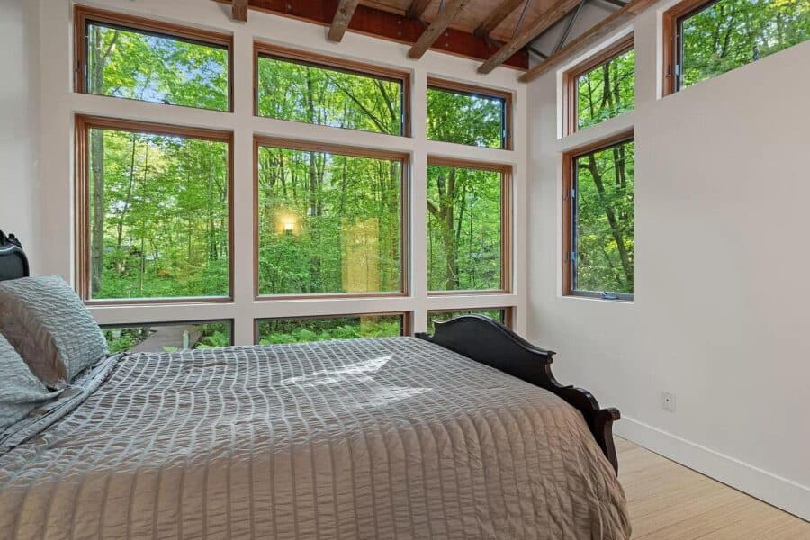 Bright bedroom with expansive windows showcasing lush green forest views.