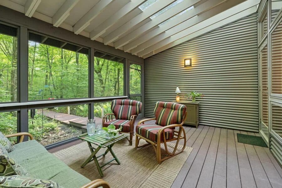 Cozy screened porch of a modern cabin in Tryon Farms, featuring comfortable seating and scenic fores.