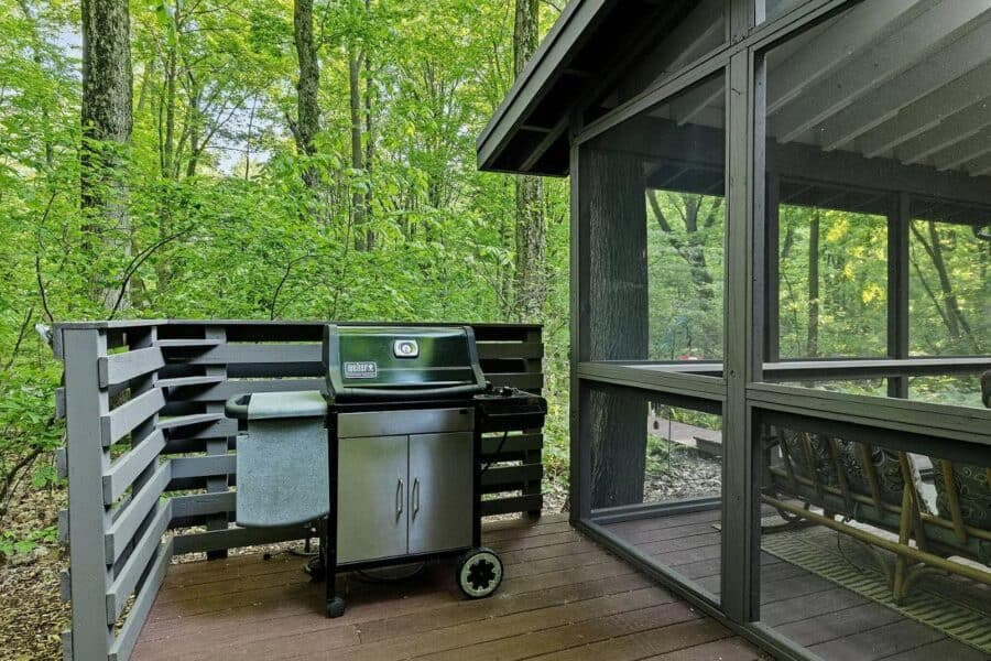 Outdoor kitchen with grill and storage on a wooden deck in a lush green forest setting.