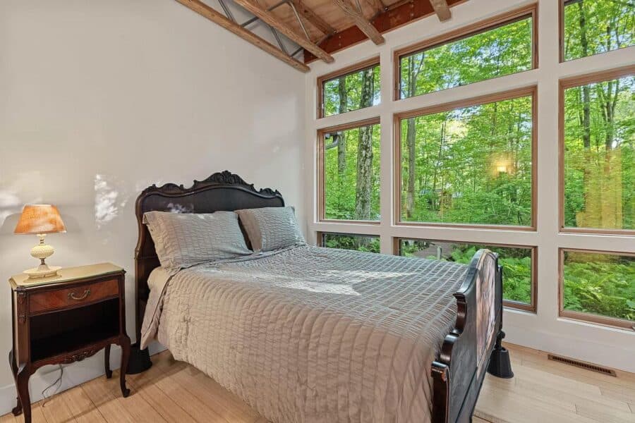 Cozy bedroom featuring large windows that showcase lush green forest scenery, perfect for a peaceful.