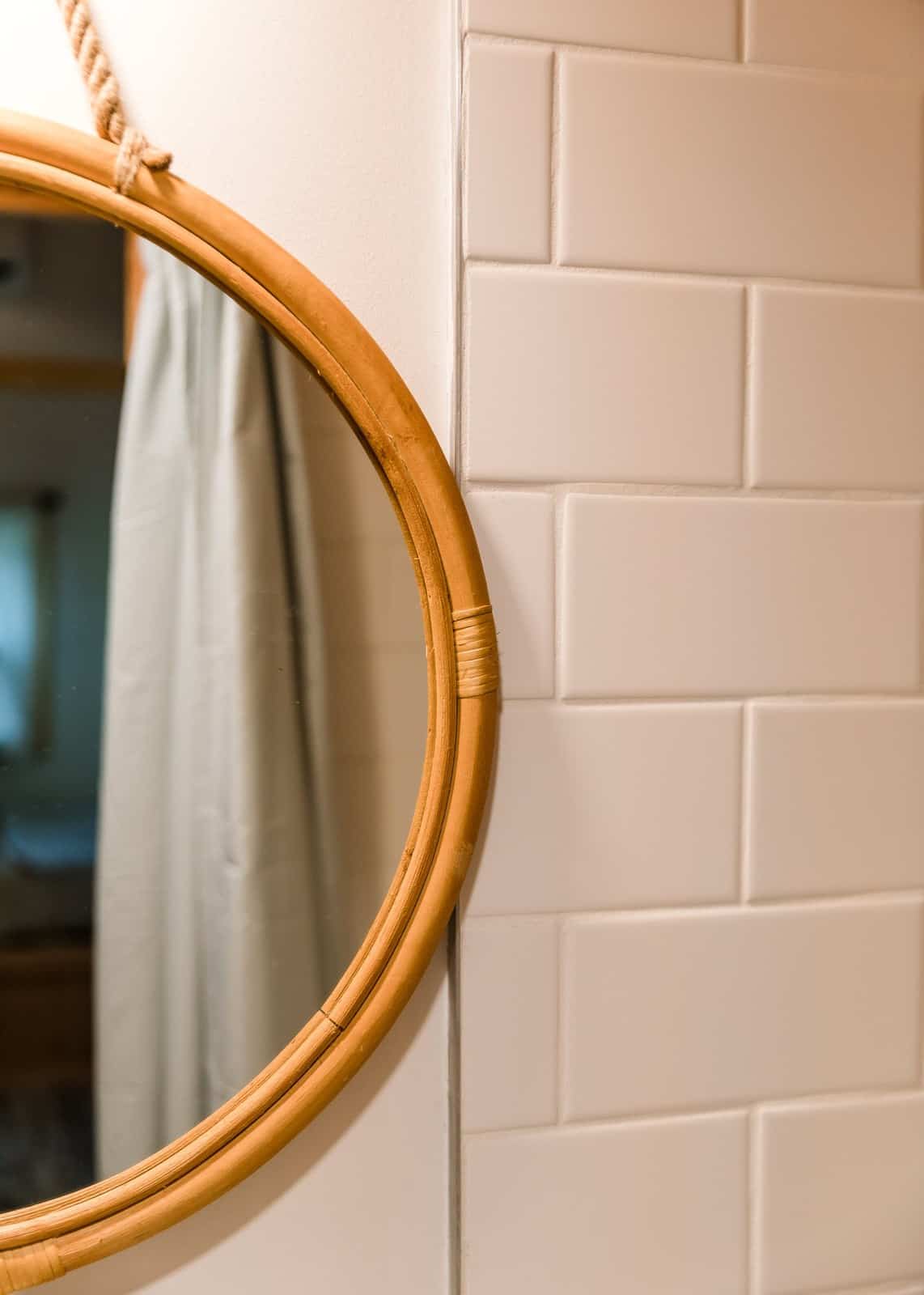 Bathroom detail in the Tulsi tiny house with a round rattan mirror against a white subway-tile wall