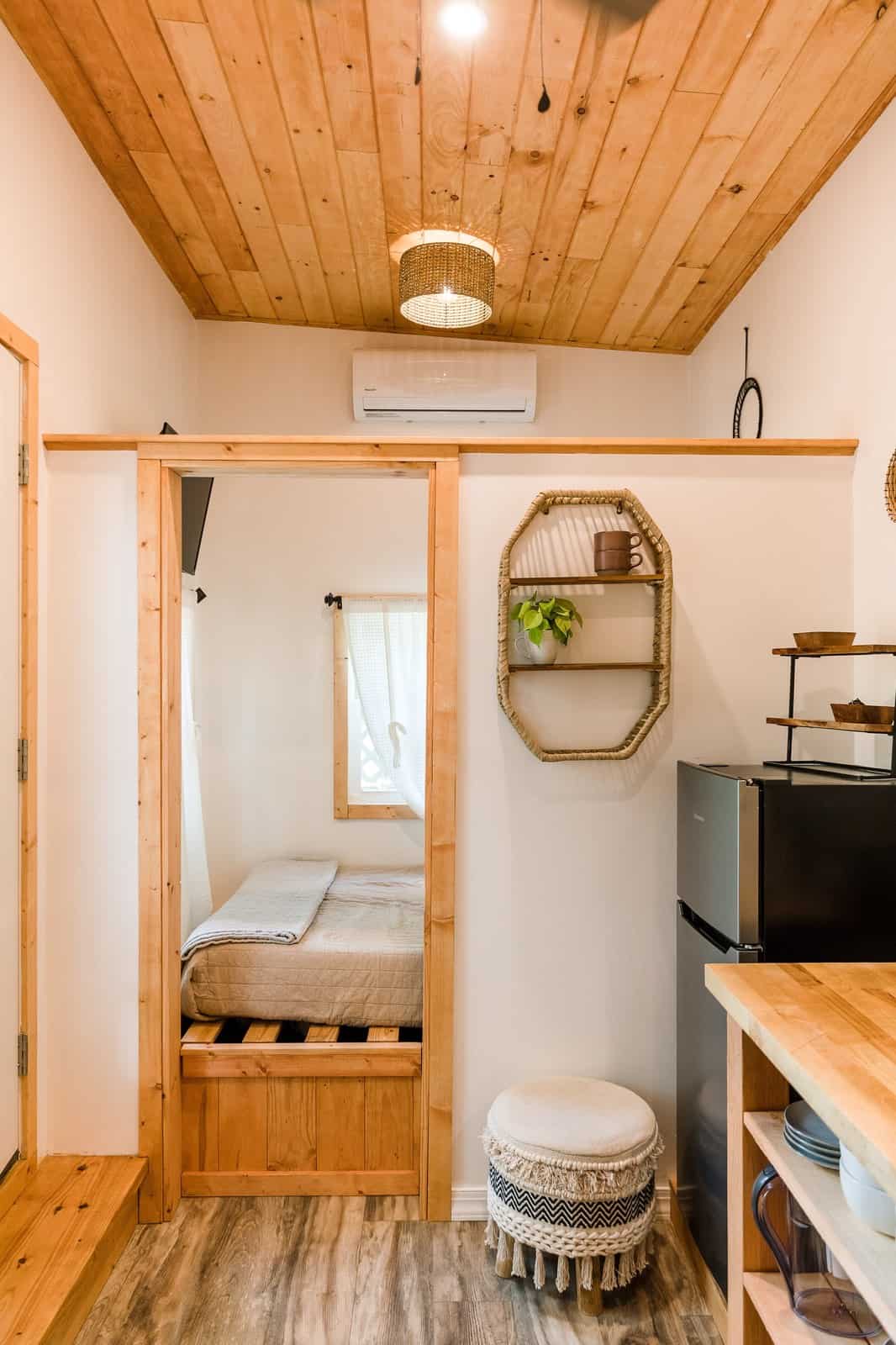 Ground-level queen bedroom doorway in the Tulsi tiny house with a mini-split above and the kitchen alongside