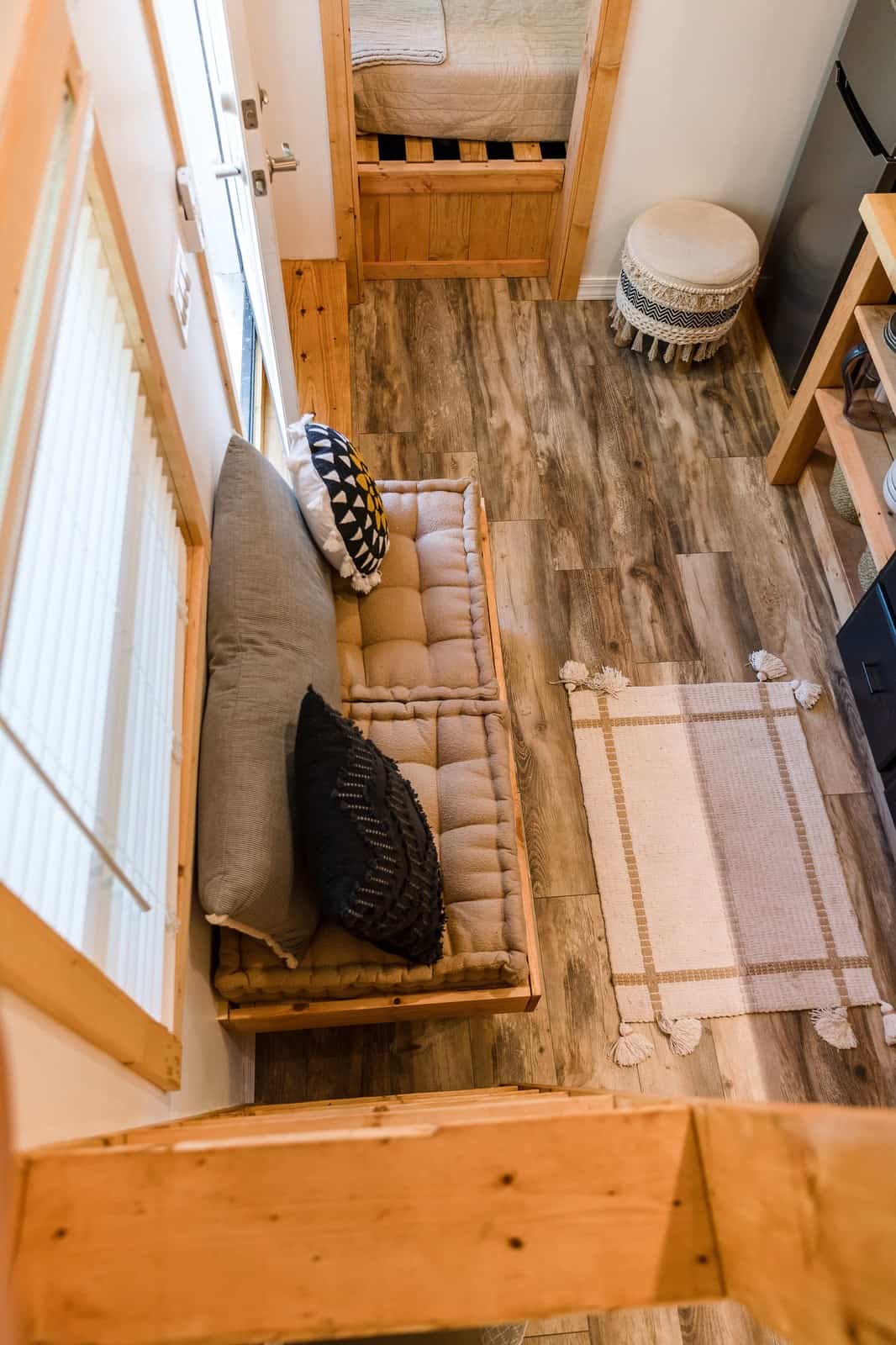 Built-in cushioned bench seating in the Tulsi tiny house, seen from the loft, with the bedroom door beyond