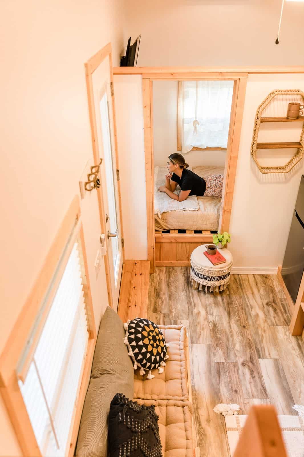 Ground-level queen bedroom in the Tulsi tiny house, viewed from the loft, with windows and a curtain