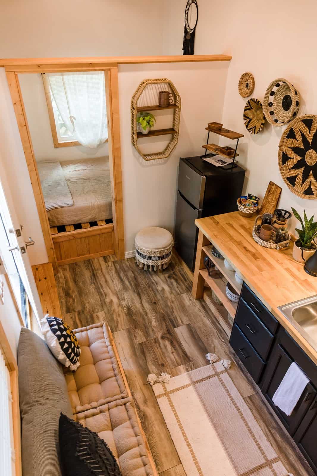 Tulsi tiny house kitchen and seating with the ground-level queen bedroom visible through an open pine door