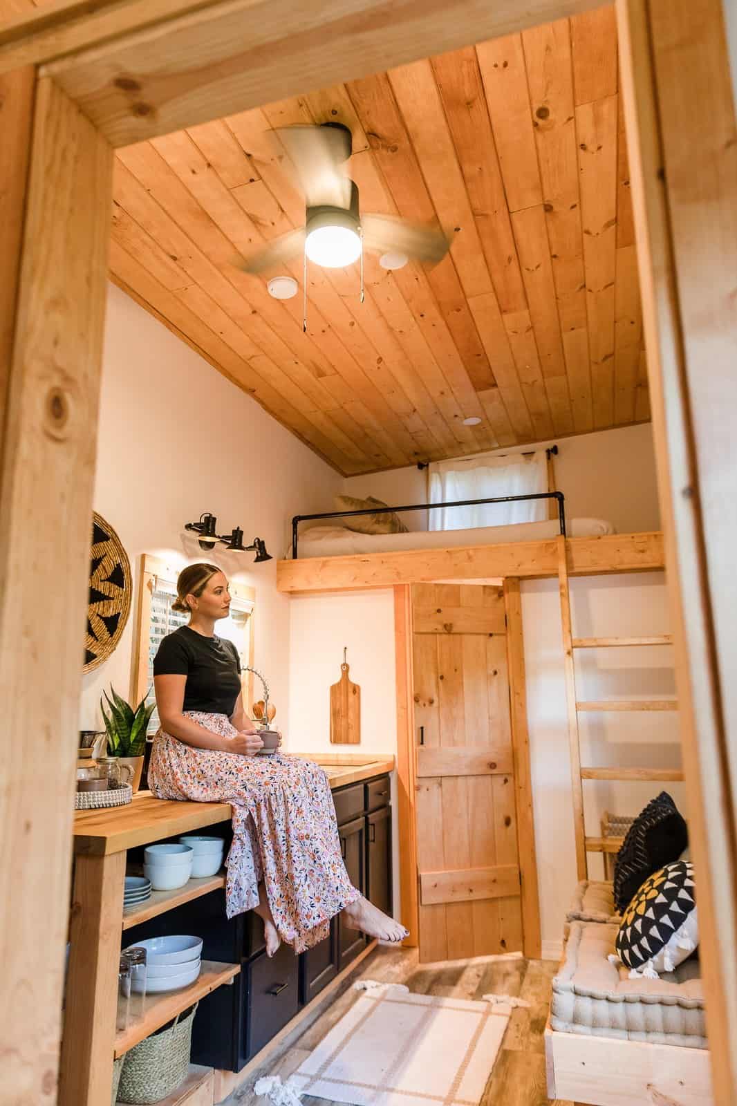 Tulsi tiny house interior with a vaulted pine ceiling, ceiling fan, sleeping loft, kitchen, and a cushioned built-in bench