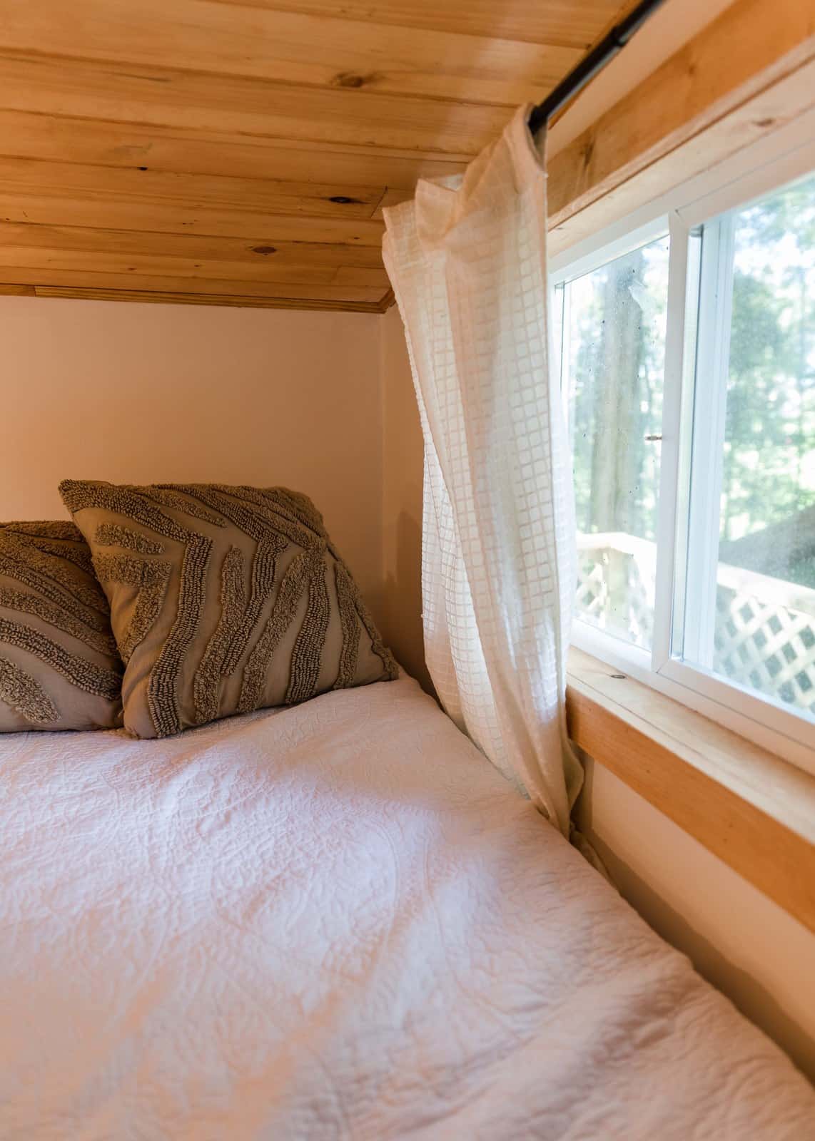 Single sleeping loft in the Tulsi tiny house with a pine ceiling and a window looking out to the trees