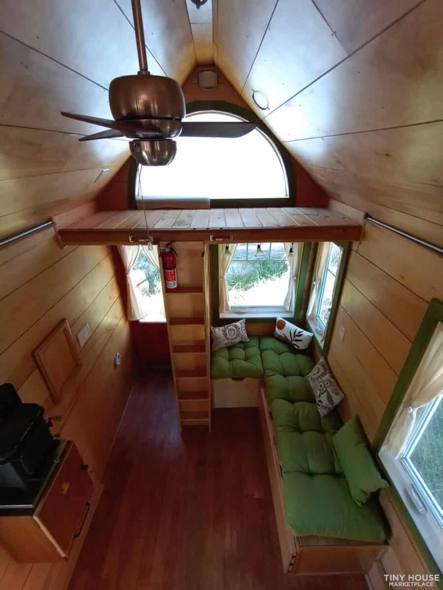 Interior view of a tiny house with a loft, green sofa, and wooden walls, showcasing efficient small.