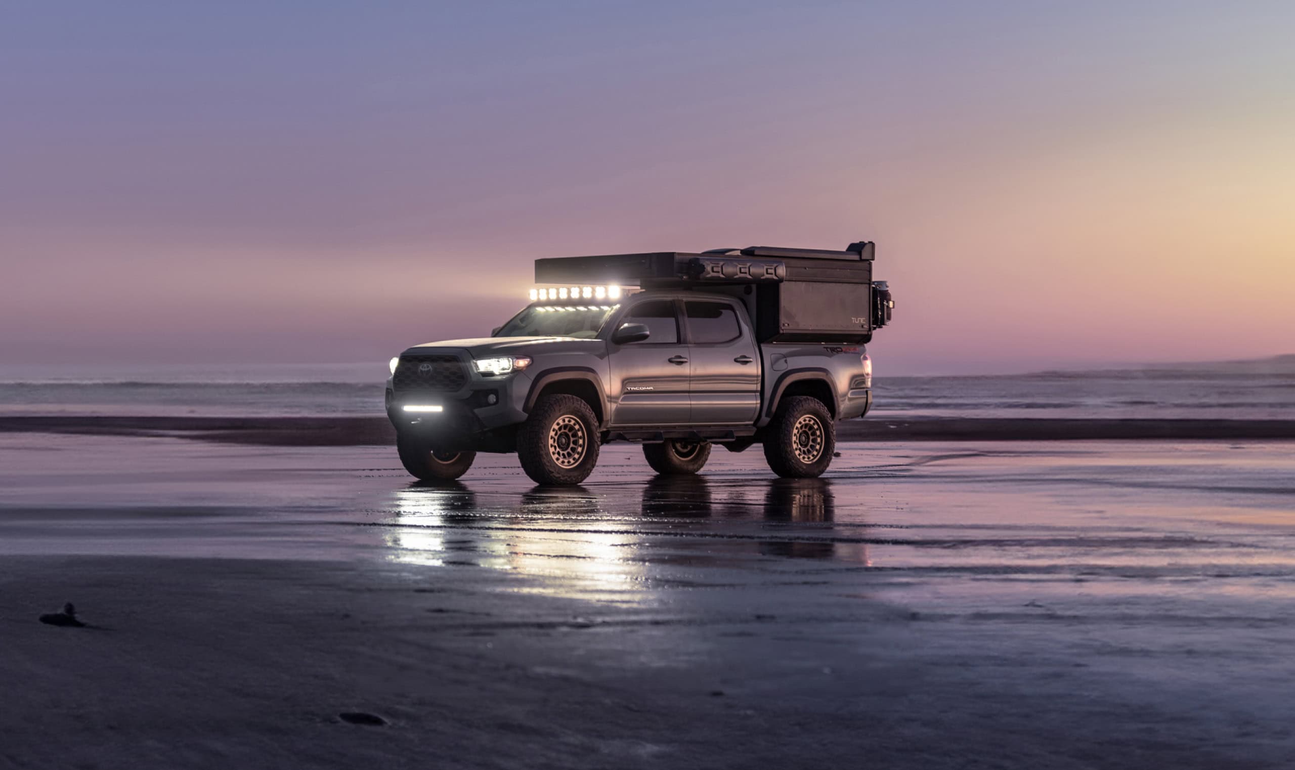 Mobile tiny house vehicle parked on beach at sunset, showcasing compact living in small spaces.