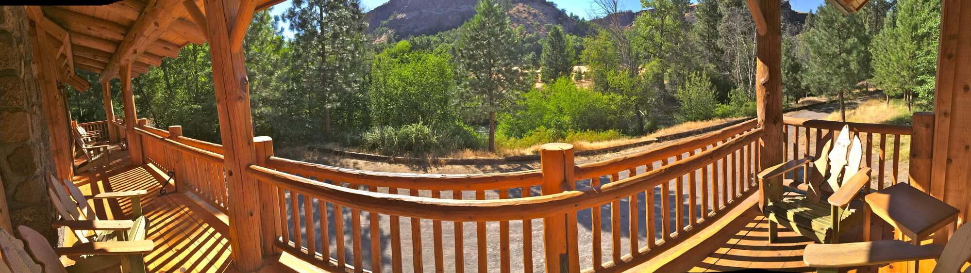 Panoramic view of the long covered deck with log railings and Adirondack chairs facing the canyon