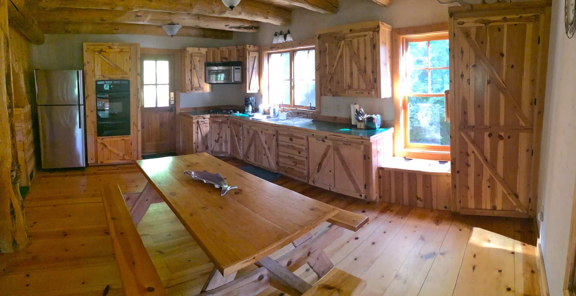 Knotty pine kitchen with barn-style cabinet doors, stainless refrigerator, and a long plank table
