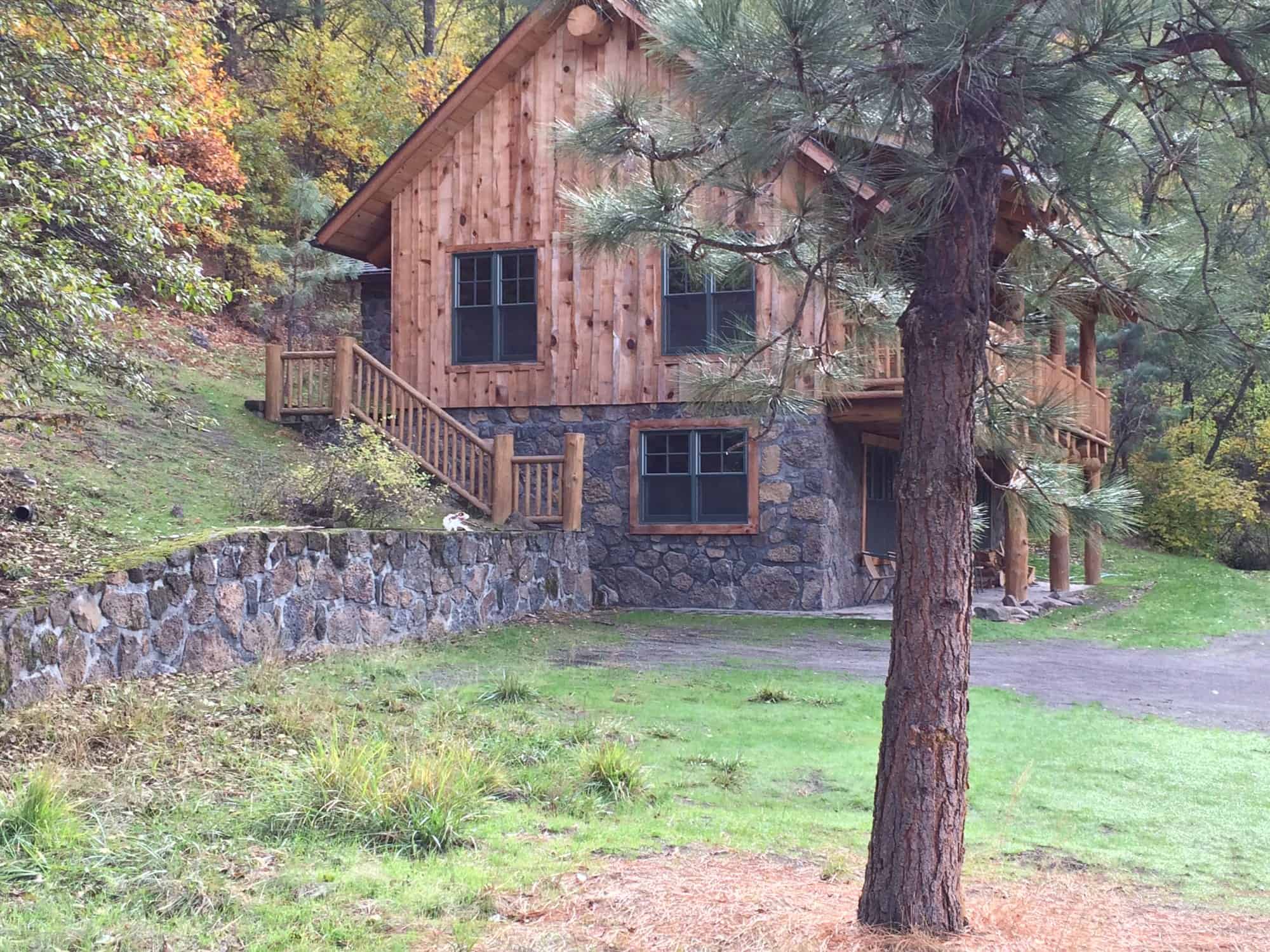 Side of the Tygh Valley log cabin showing its stone lower level, stairs to the deck, and stone retaining wall