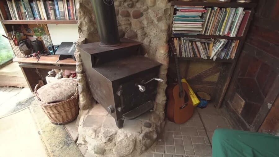 Salvaged barn wood stove set in a cob and stone surround between bookshelves