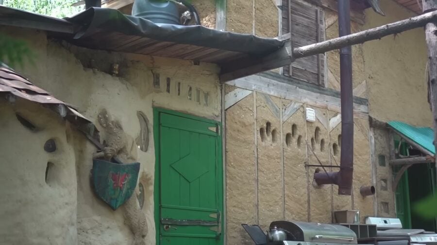 Cob outbuilding with sculpted earthen walls, bottle niches and a green door
